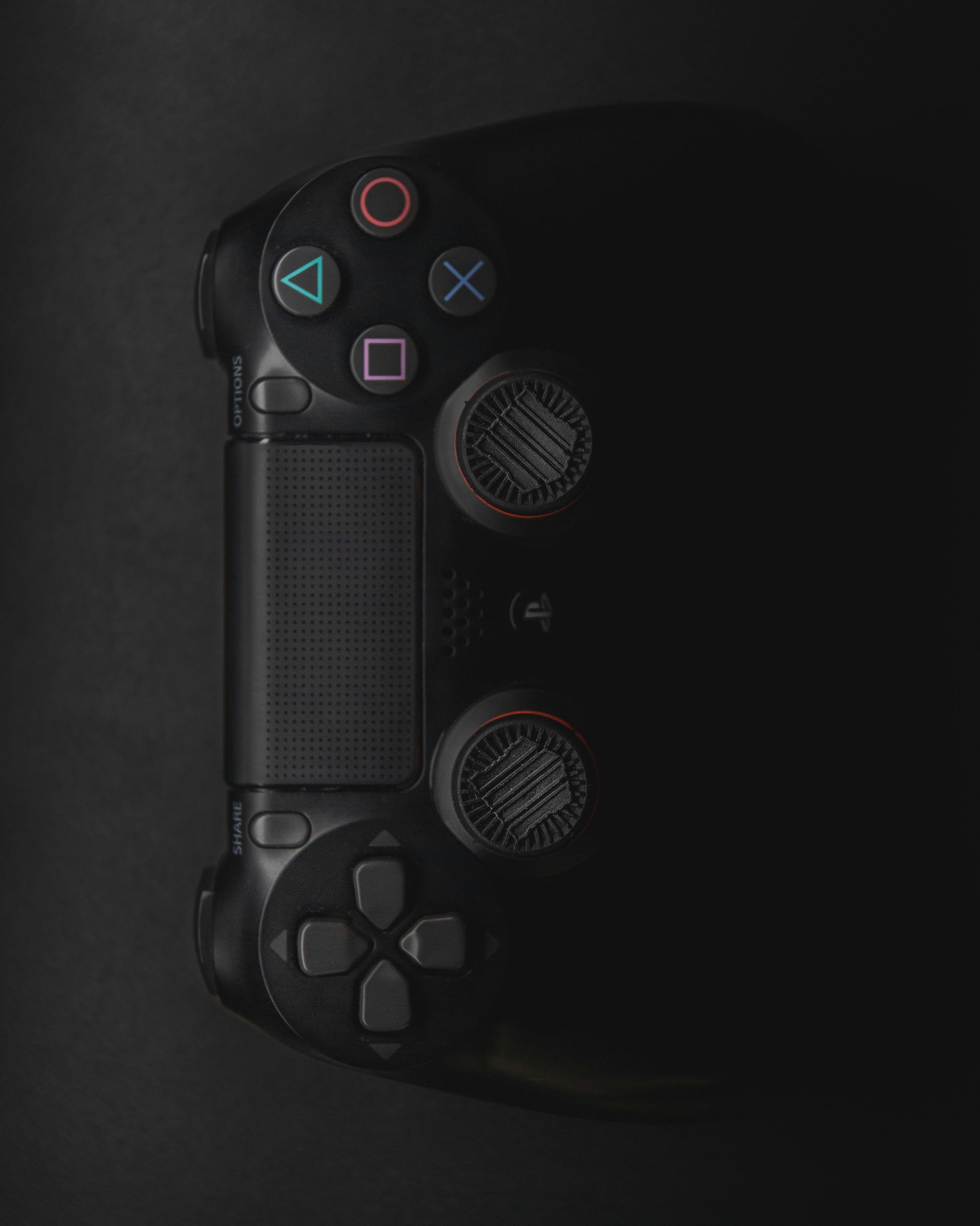 Moody close-up of a black gaming controller in low light with colorful buttons.